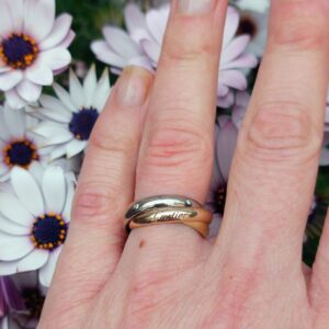 Cartier, bague Trinity modèle Classique, 5 diamants. Bague Trinity Cartier portée à l'annulaire. Les trois anneaux entrelacés en or jaune, or blanc et or rose ainsi que la signature Cartier sont clairement visibles. Cinq diamants brillants sur l'anneau central.